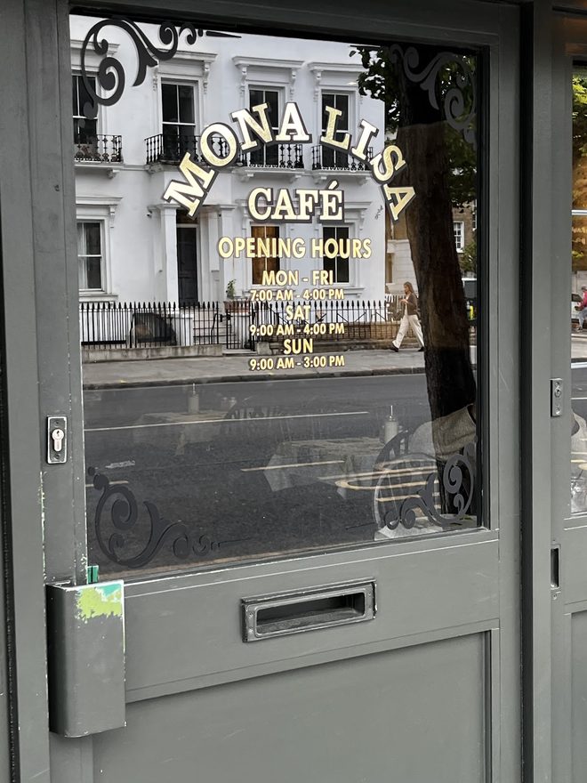 The glass entrance door with the cafe name and hours in gold lettering. Crop the burned-in caption text off the edge.